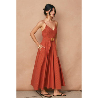 Woman wearing a rust-colored dress with a belt against a beige wall.