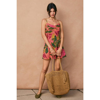 Woman in a floral dress holding a woven bag against a beige background