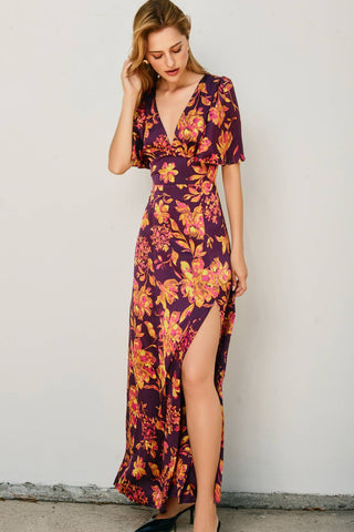 Woman wearing a floral dress with a high slit against a plain background