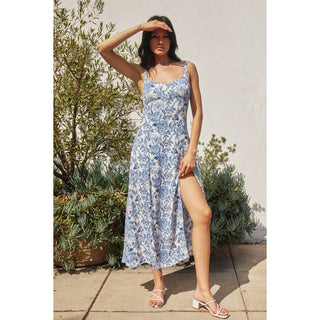 Woman wearing a blue floral dress standing outdoors with plants in the background